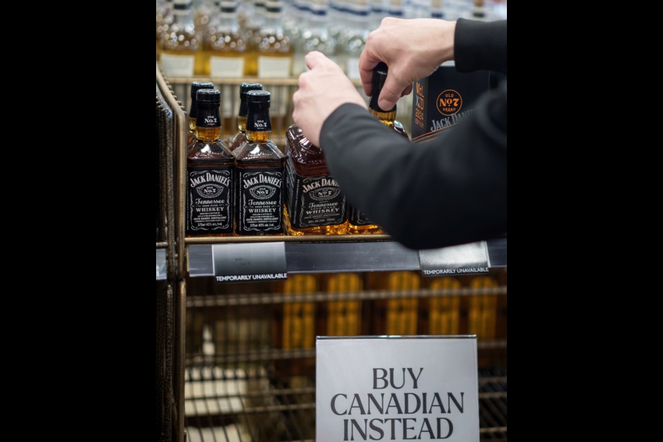 A B.C. Liquor Store employee demonstrates removing bottles of American whiskey for media before a news conference in Vancouver, B.C., Sunday, Feb. 2, 2025. (Ethan Cairns/The Canadian Press via AP)