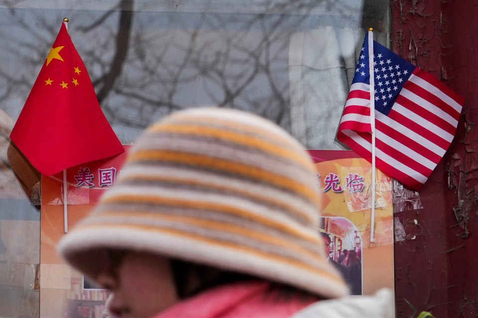 A woman walks by the Chinese and U.S. national flags on display outside a souvenir shop in Beijing on Jan. 31, 2025. (AP Photo/Andy Wong)