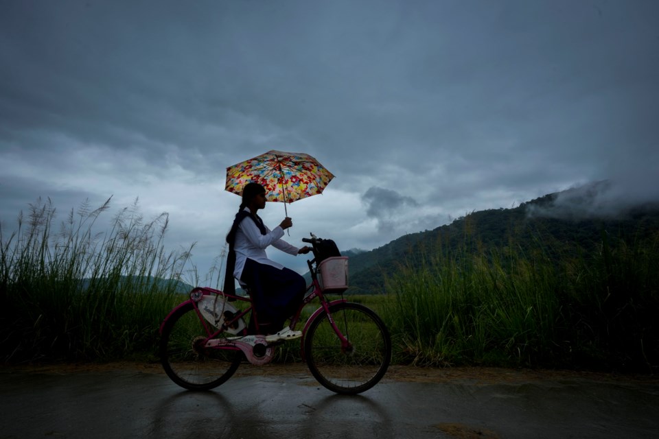 FILE - A school girl with an umbrella rides on her bicycle to school during a monsoon rain as clouds hover over the sky on the outskirts of Guwahati, India, June 20, 2024 (AP Photo/Anupam Nath, File)