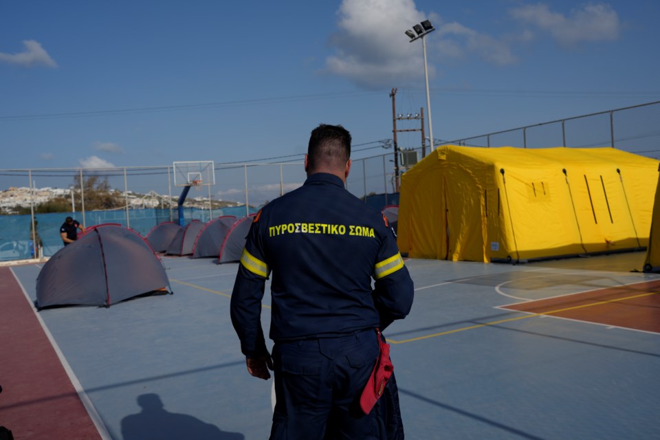 A firefighter walks next to tents set up at a basketball court to accommodate Fire Service rescuers as Greek authorities is taking emergency measures in response to intense seismic activity on the popular Aegean Sea holiday island of Santorini, southern Greece, Monday, Feb. 3, 2025. (AP Photo/Petros Giannakouris)