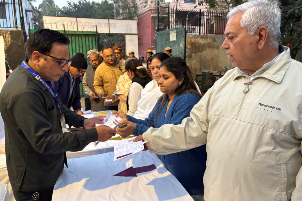 A polling officer checks the identity cards of people before they cast their votes for the capital’s state legislature election at a polling booth in New Delhi, India, Wednesday, Feb. 5, 2025. (AP Photo/Shonal Ganguly)