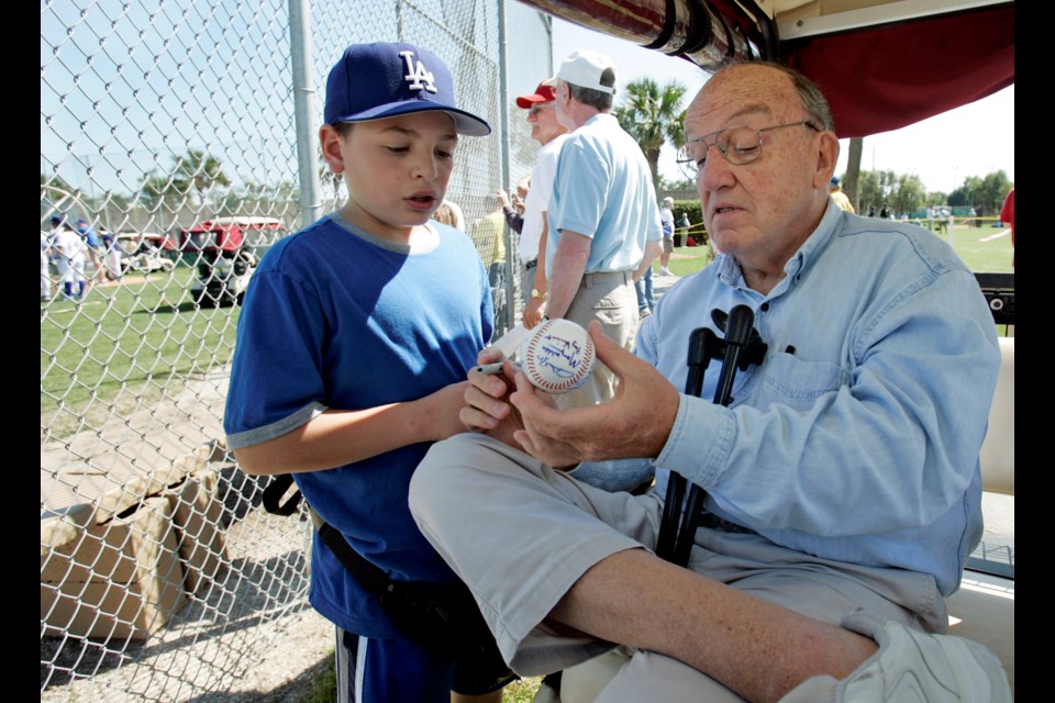 FILE - Former Major League Baseball Commissioner Fay Vincent signs an autograph for Louis Carrons, 12, of Rancho Cucamonga, Calif., during Los Angeles Dodgers baseball spring training in Vero Beach, Fla., March 1, 2006. (AP Photo/Richard Drew, File)