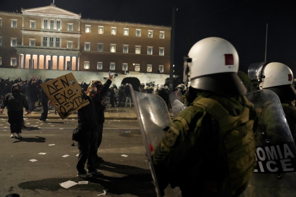 Protesters raise their hands as riot police operate during clashes, as the Greek opposition parties have challenged the country's center-right government with a censure motion in parliament over a devastating rail disaster nearly two years ago, in Athens, Wednesday, March 5, 2025. The placard reads "I have no oxygen", a phrase which a victim of the deadly train accident, used in a phone call to the emergency services. (AP Photo/Petros Giannakouris)