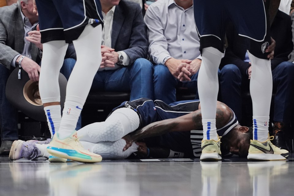 Dallas Mavericks' Kyrie Irving holds onto his leg after suffering an unknown injury as teammates stand by in the first half of an NBA basketball game against the Sacramento Kings in Dallas, Monday, March 3, 2025. (AP Photo/Tony Gutierrez)