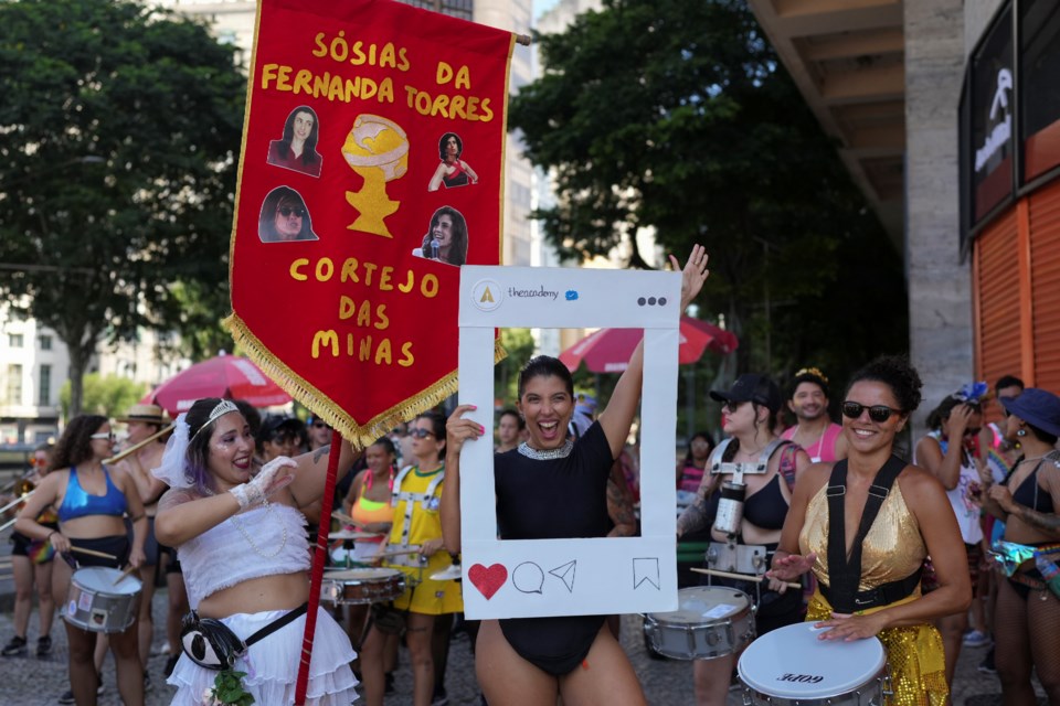 A reveler dressed as Oscar-nominated actress Fernanda Torres holds a cutout depicting theacademy Instagram account, next to a banner labeled in Portuguese; "Fernanda Torres' Impersonators", during a pre-Carnival street party where some dressed as Torres' beloved TV characters, in Rio de Janeiro, Sunday, Feb. 23, 2025. (AP Photo/Silvia Izquierdo)