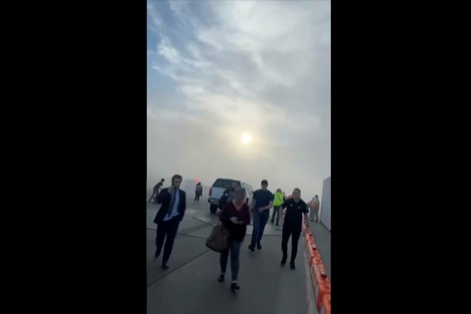 In this image taken from video provided by Justus Rainey, passengers move away from a plane as smoke surrounded the aircraft, in Denver, Thursday, March 13, 2025. (Justus Rainey via AP)