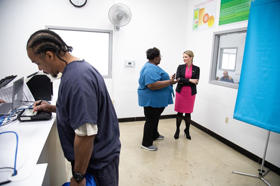 Secretary Benson (right) speaks with MDOS Deputy Legal Director Khyla Craine while a returning citizen at Parnall Correctional Facility completes the steps to secure his ID documents