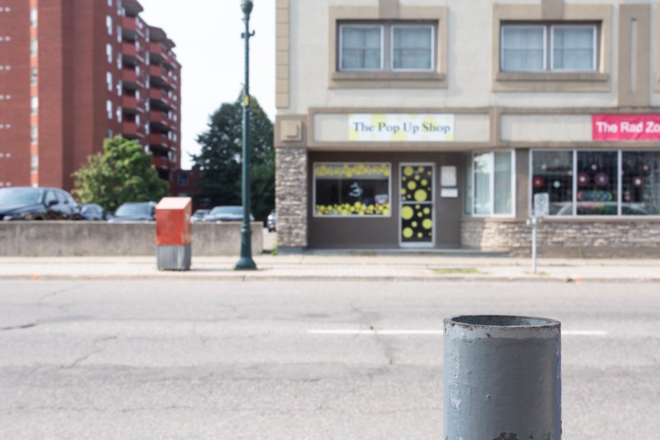 A metal pole that once held a parking meter now stands empty on Queen Street East, while the meters across the street have also been removed.