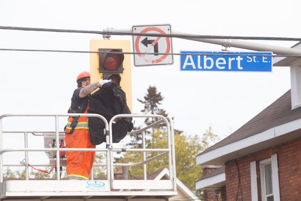 A city worker on a scissor lift removes the fabric cover from a traffic lights at the intersection of Albert and Elgin streets on Wednesday. A decision was made to restore the signals after a months-long traffic study.