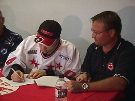 <b>McInerney signs his OHL contract under the eye of general manager Dave Torrie.