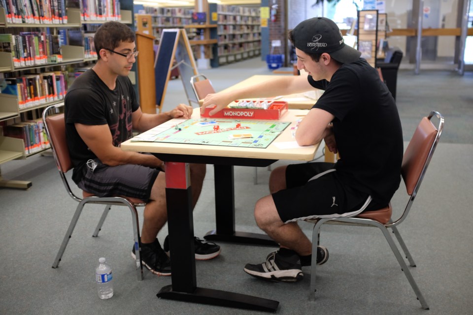 (From left) Ethan Mogani and Allan Hirchberg got out of the heat on Wednesday by playing a game of Monopoly at the Centennial Public LIbrary. Photo by Jeff Klassen for SooToday