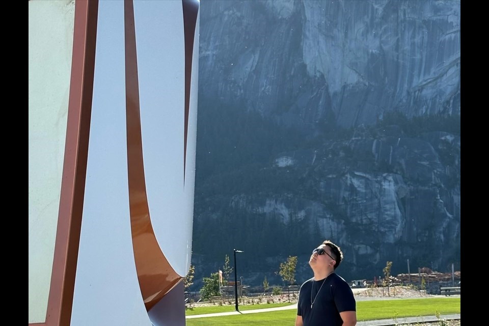 James Harry, a Sḵwx̱wú7mesh 
artist whose work is featured at the Squamish Arts Festival. Here is stands with Welcome Gate on the oceanfront in Squamish.