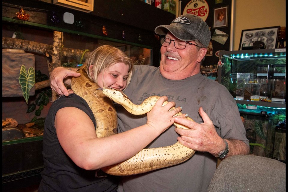 QUITE THE HANDFUL — John DeJordy, right, and his daughter Amber try to wrangle Nyx the snake into a photogenic position. Nyx was more interested in getting back to the luxury habitat behind them. KEVIN MA/St. Albert Gazette