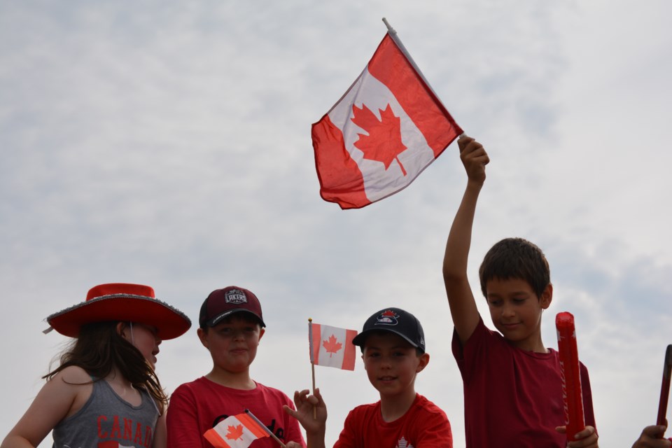 Kids hold up Canadian flags on the Orr Insurance float as part of the 2023 Stratford Canada Day parade.