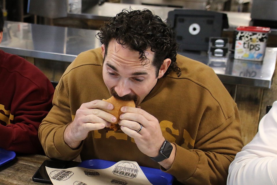 Andre Vaillant takes a bite out of the Prospector Burger Barn's offering for the 2022 Novemburger competition on Tuesday, Nov. 1, 2022. (Leith Dunick, tbnewswatch.com)