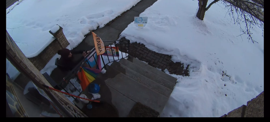 A screenshot from a home security camera showing a person vandalizing Pride items at a home. 