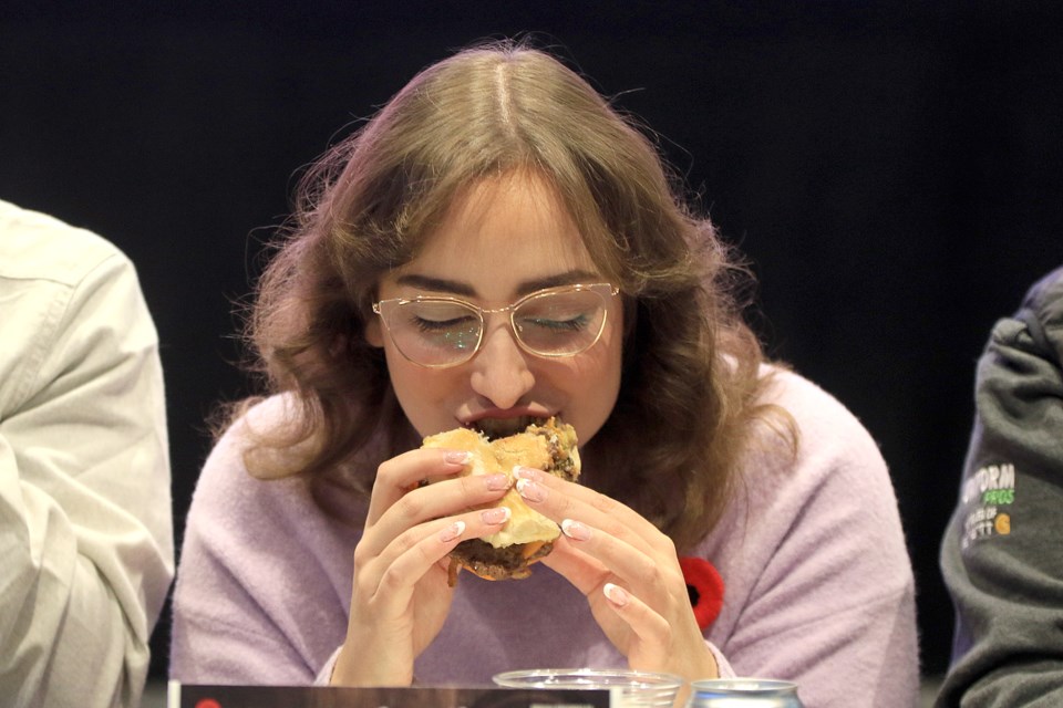 Thunder Bay Television's Hailey Perrault devours a Novemburger offering on Friday, Nov. 1, 2024 at the Outpost. Kicking off the 6th annual Novemburger campaign. (Leith Dunick, tbnewswatch.com)