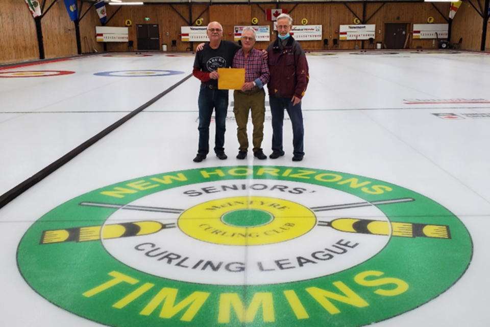 The Timmins Food Bank's Jim Young accepts a donation from New Horizons Seniors’ Curling League president Wayne Jaszan and member Dave Montreuil.