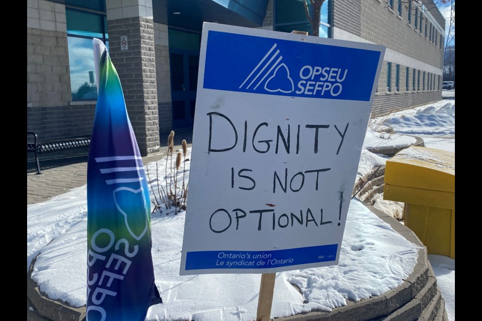 A sign reading "Dignity is not optional" sits in a snowbank in front of the Timmins Public Library.