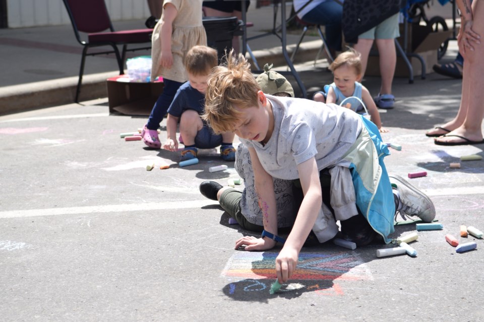 Ben Ambrosio, 9, from Edmonton, whose family has a weekend cabin in Birch Cove, draws the Pride flag in front in chalk in front of the Barrhead United Church as part of their OutProud booth.