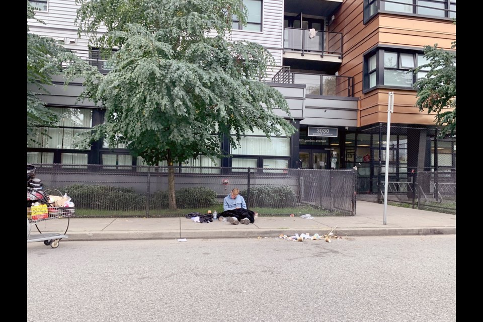 A man sits on the sidewalk outside of 3030 Gordon Ave., in Coquitlam, at 1 p.m. on Sept. 17, 2024.