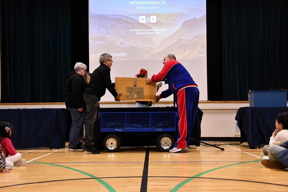 Harbour View Elementary principal Daren Fridge, with former administrators and teachers, hauls the box from the wagon onto the blue-covered table for the big reveal on Jan. 24, 2025.