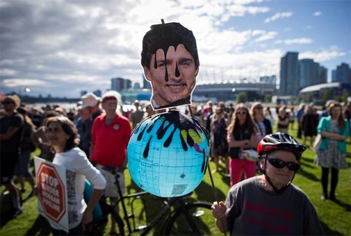  A protester holds a photo of Prime Minister Justin Trudeau and a representation of the globe covered in oil during a protest against the Kinder Morgan Trans Mountain Pipeline expansion in Vancouver, B.C., on Tuesday May 29, 2018. The federal Liberal government is spending $4.5 billion to buy Trans Mountain and all of Kinder Morgan Canada's core assets, Finance Minister Bill Morneau said Tuesday as he unveiled the government's long-awaited, big-budget strategy to save the plan to expand the oilsands pipeline. THE CANADIAN PRESS/Darryl Dyck