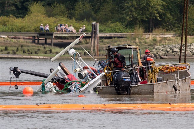  Workers watch as a capsized tugboat is lifted from the Fraser river between 鶹ýӳand Richmond, B.C., on Wednesday, August 15, 2018. THE CANADIAN PRESS/Ben Nelms