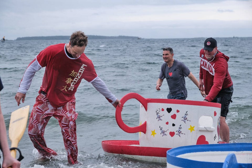 Olympic medallists Dominic Seiterle, left, and Adam Kreek, right, help drag a teacup as Oak Bay Mayor Kevin Murdoch walks triumphantly back to shore on June 2, 2024. TIMES COLONIST 