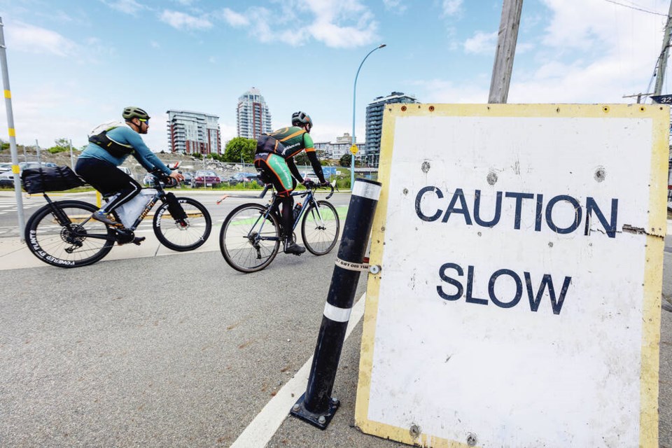 Cyclists zip past a makeshift sign on Harbour Road near the on and off ramp to the Johnson Street Bridge, where a mixed-use lane crosses a sidewalk.  DARREN STONE, TIMES COLONIST 