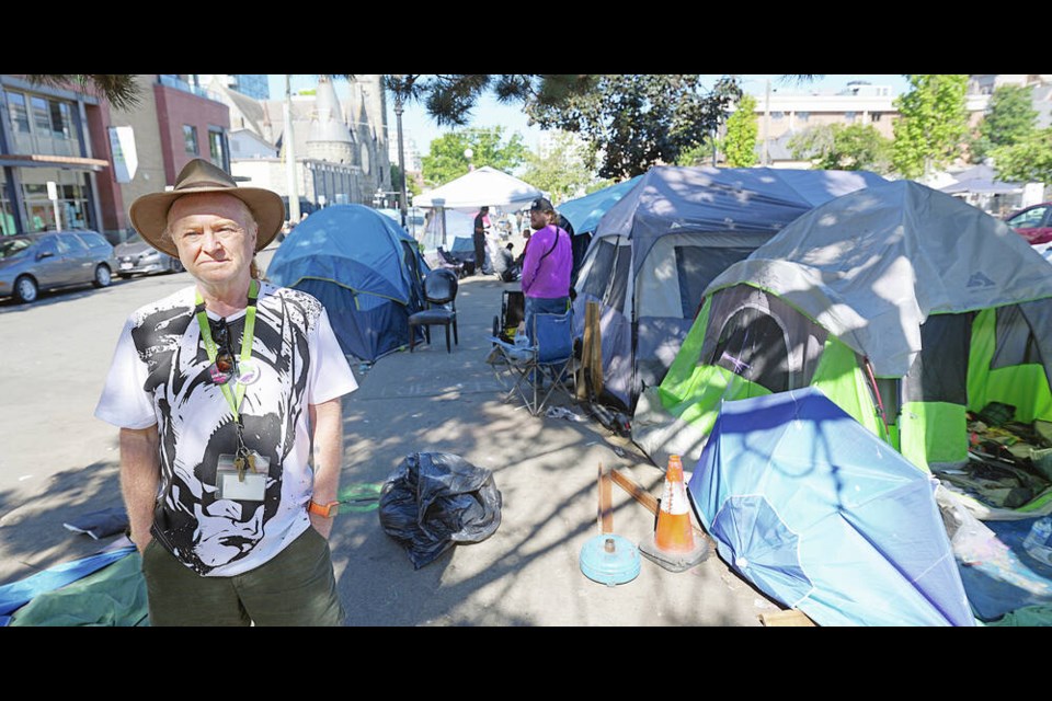 Our Place communications director Grant McKenzie stands among tents outside the agency on Pandora Avenue on Tuesday. Regulating body heat is particularly challenging for those who use fentanyl or other opioids, he says. “If people are opioid users, it can be quite easy for them to curl up in a ball somewhere with the sun beating down on them.” ADRIAN LAM, TIMES COLONIST 